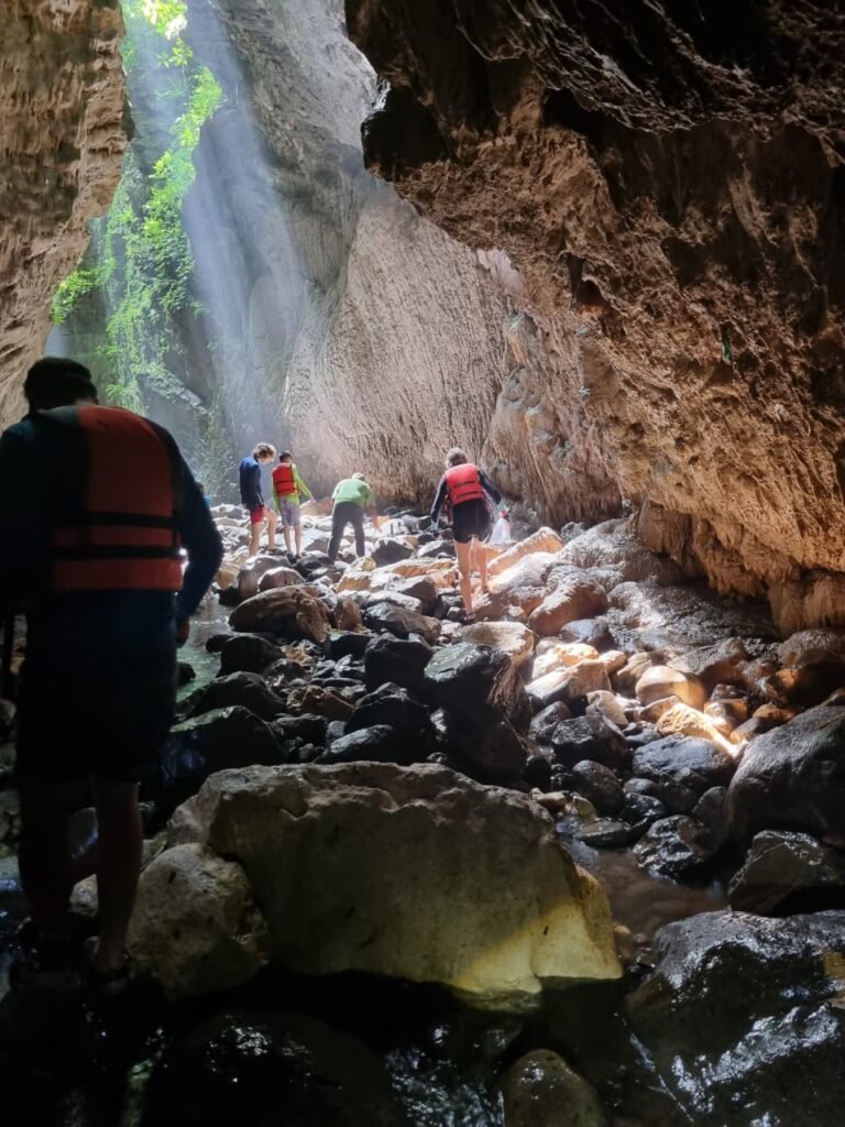 Visitors in life vests walking over rocks at the entrance canyon of the Bayano caves, lit by natural light