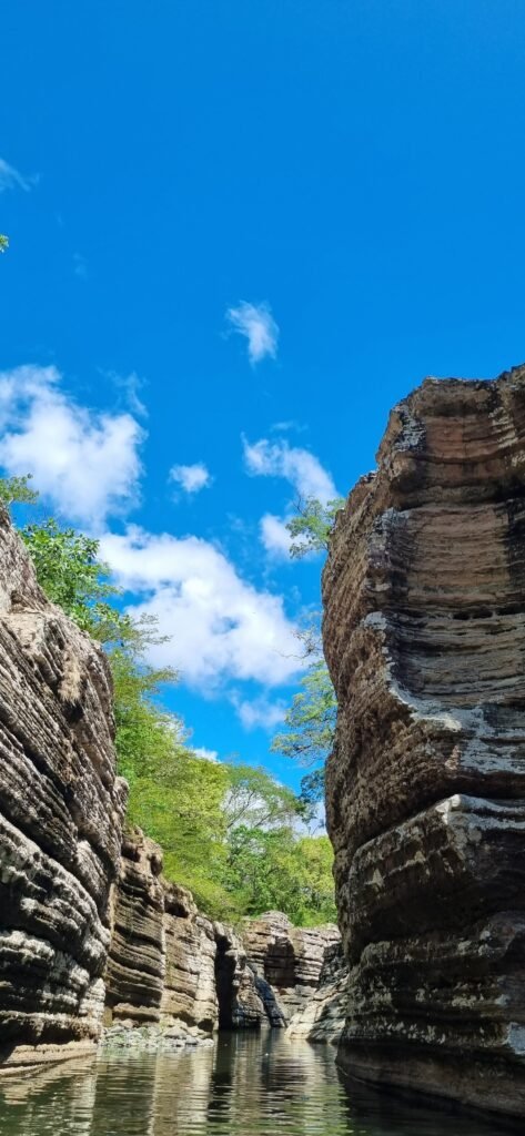 Layered rock formations of the Cajones de Chame canyon rising above calm green water