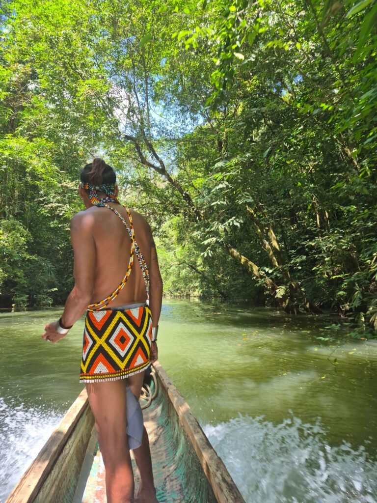 Emberá guide in traditional beaded dress standing on a piragua dugout canoe navigating the Chagres river