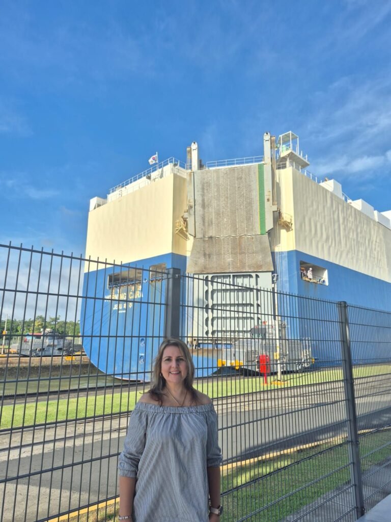 Visitor at the fence beside a car carrier ship in a Panama Canal lock chamber, with a towing locomotive alongside