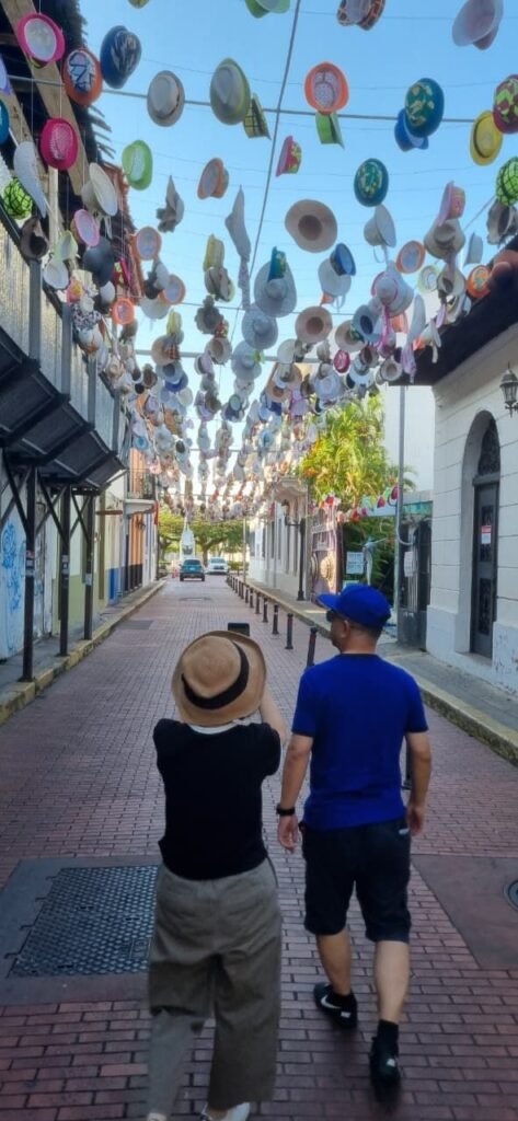 Couple walking beneath a colorful canopy of hanging hats on a historic street in Casco Viejo, Panama City